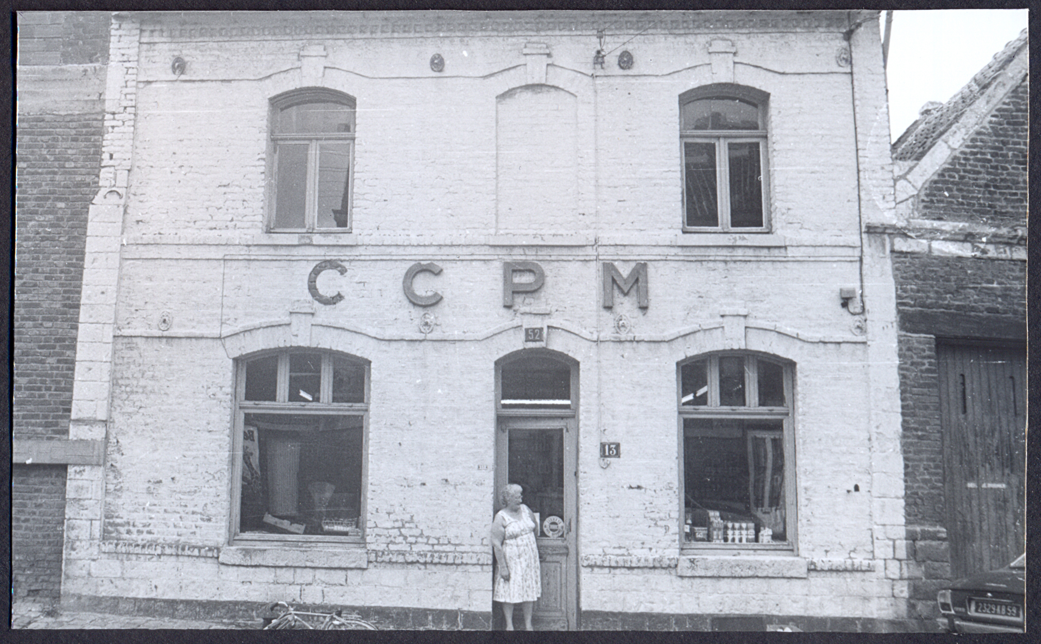 Commerçante posant devant la façade d’une coopérative minière : tirage photographique, Lewarde (Nord), 1982.
