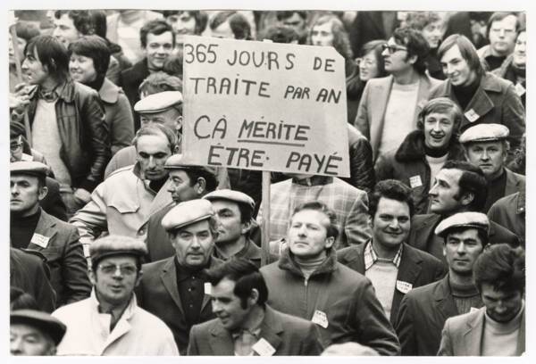 Agriculteurs brandissant une pancarte « 365 jours de traite par an, ça mérite être payé » lors d’une manifestation : photographie, sans lieu ni date.